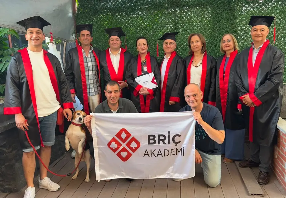 Kursları tamamlayan öğrenciler cübbe ve keple Briç Akademi bayrağıyla